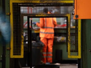 An operative wearing orange PPE sorting waste material in a Materials Recycling Facility