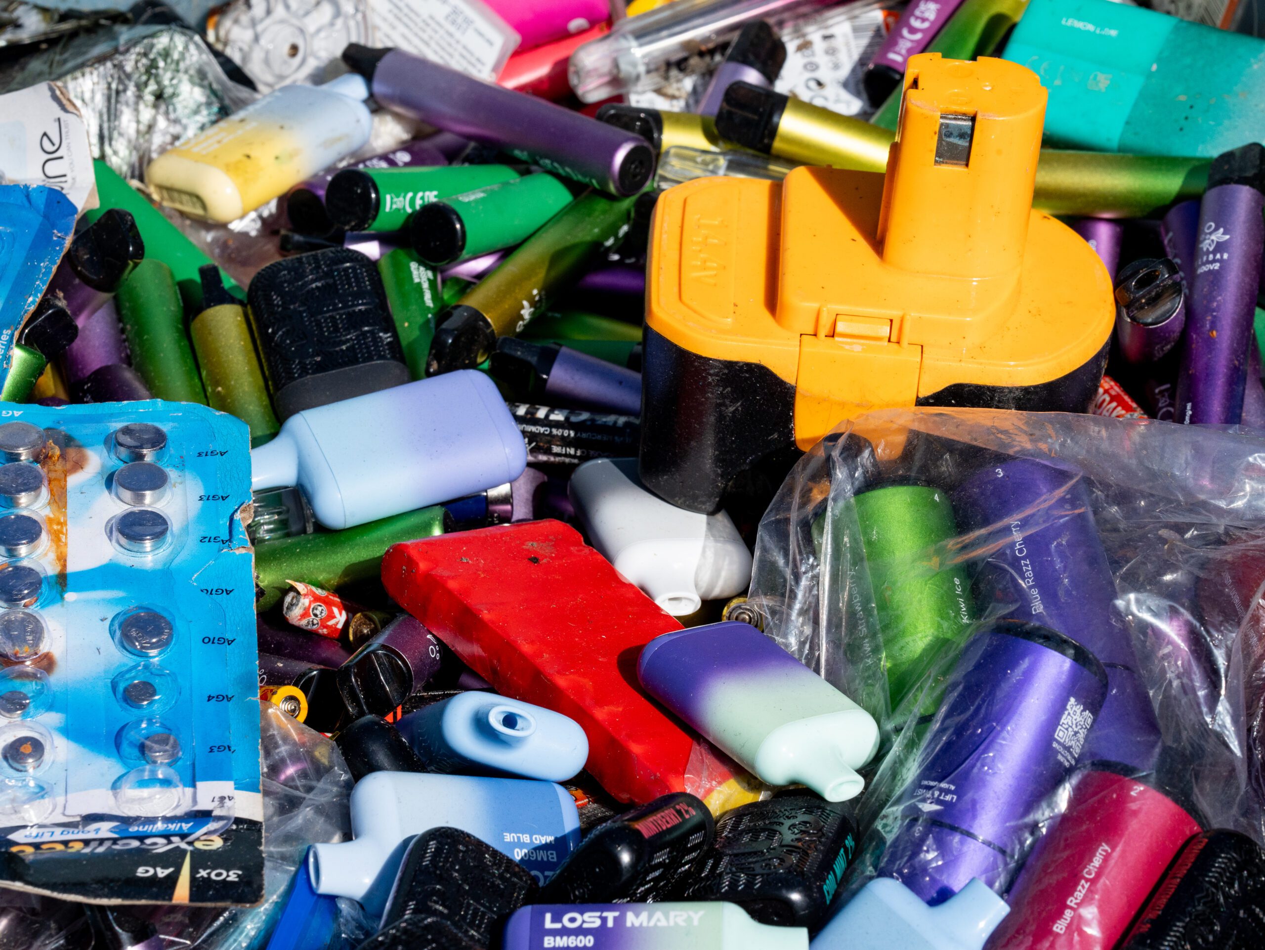 A collection of various types of batteries and disposable vape devices in a recycling container